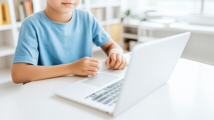 Boy wearing blue t-shirt using laptop doing school homework and studying online sitting in his bright room during daytime. Using computer at home and researching information on the Internet.