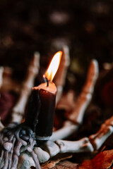 Halloween creepy atmosphere.Burning Candle on Skeleton Hand with Autumn Leaves.Spooky Halloween...