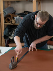 Leatherworker measuring and cutting leather in workshop. 