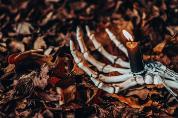 Burning Candle on Skeleton Hand with Autumn Leaves.Spooky Halloween Candlestick. Halloween...