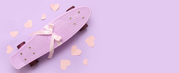 Skateboard with bow and paper hearts on lilac background with space for text, top view