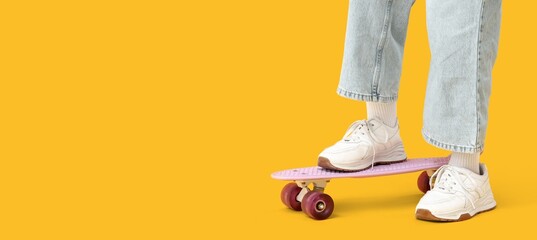 Legs of teenager in sneakers, jeans and with skateboard on yellow background with space for text