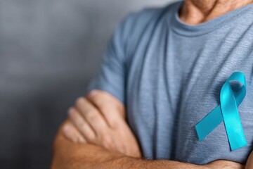 Senior man is wearing light blue t shirt with teal awareness ribbon pinned on his chest, supporting human trafficking and sexual assault prevention