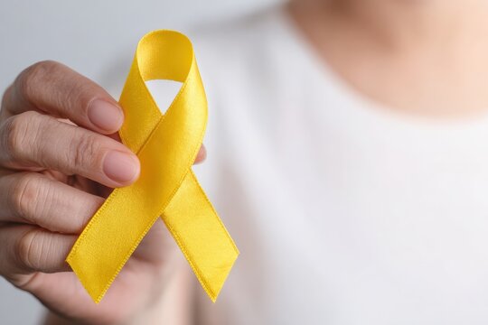 Close up of woman holding yellow ribbon showing support for Bone Cancer, Suicide Prevention and troops deployed - Powered by Adobe