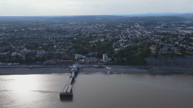 Aerial shot looking at Penarth pier and the beach pans left following the coastline, lots of people and cars can be seen moving and the town is seen in the background, Wales, UK, 4K, 60fps