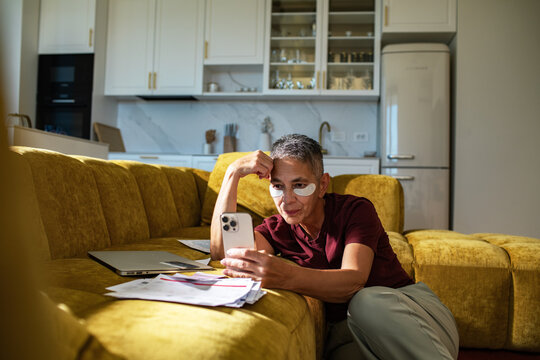 Senior woman with eye patches relaxing on sofa while reviewing bills at home