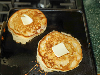 View of pancakes on a hot griddle with a pat of butter on top.