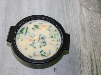 A round black plastic to go box with gnocchi soup and view of a clear lid on the corner.
