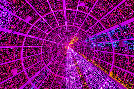 Interior view from below of a circular Christmas structure with pink, purple, yellow and blue lights forming a symmetrical grid pattern