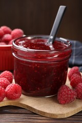 Sweet raspberry jam in glass jar and berries on table, closeup
