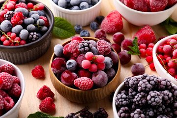 Different ripe frozen berries and mint leaves on light wooden table, closeup