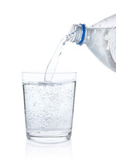 Pouring refreshing soda water from bottle into glass on white background