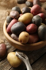 Different types of potatoes in bowl and peeler on wooden table, closeup