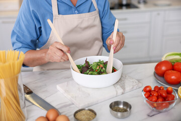 Senior woman cooking salad at white marble table in kitchen, closeup