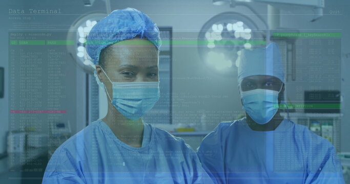 Standing two surgeons in blue scrubs examining vitals in operating room, with lights and monitors