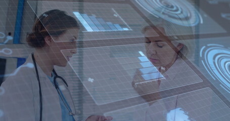 Analyzing two female doctors gesturing at holographic charts in clinic, with stethoscope and pen