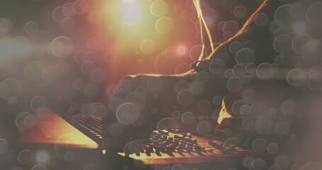 Twisting DJ arm in dark sleeve adjusting mixer knobs on nightclub stage, with warm light bokeh