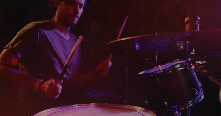 Playing male drummer wearing grey tshirt and jeans behind drum kit at music venue, copy space