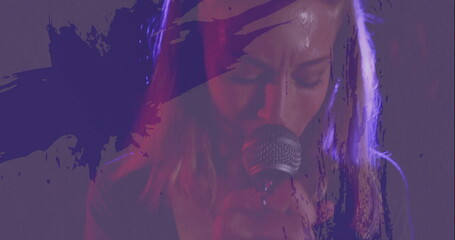 Performing singer holding microphone onstage under purple and red lights, with abstract overlays