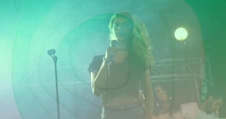 Singing lead singer holding wired microphone at concert stage, with spotlights fog haze truss