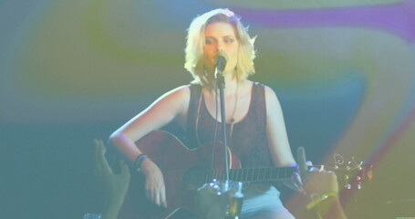 Teenage singer playing acoustic guitar on club stage, with mic stand and colored lights