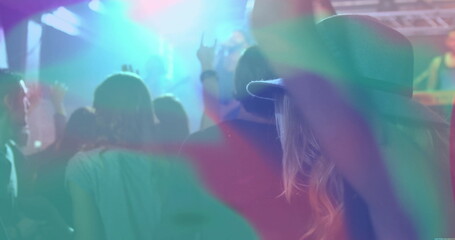 Raising fan wearing wide-brimmed hat making rock sign in light beams at concert venue, copy space
