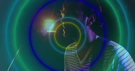 Singing musician wearing V-neck shirt on stage, with mic, backlight and neon rings, copy space