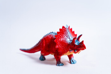 Red triceratops dinosaur toy standing on white background