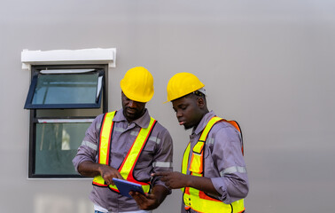 Two young black construction workers wearing protective helmets use a digital tablet and work while...
