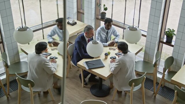 Reflection in mirror of three intercultural white collar workers sitting by table in cafe and discussing main points of their reports before business conference