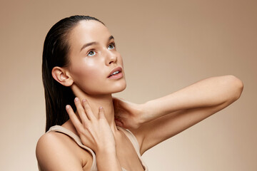 Young woman with wet hair looking upwards against a beige background, expressing serenity and...