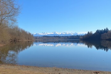 Tranquil Lake Scene with Snow-Capped Mountains Reflected in Calm Waters Under Clear Blue Sky in a Serene Natural Setting