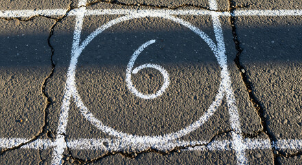 Close-up of chalk drawn hopscotch grid number six in a circle on asphalt playground surface with light shadow