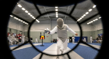 Fencer engaged in a competitive duel during a sports match on a blue and white court viewed through a wire mesh