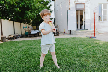 Happy boy playing outdoors with a toy, enjoying a sunny day in the garden surrounded by greenery and bright sunlight, conveying a sense of childhood joy.