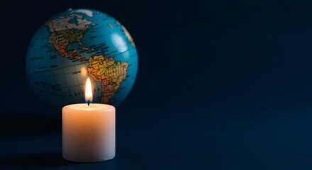 Fototapeta premium A small lit candle in front of the globe, plain background with copy space, symbol of prayer for the earth.