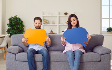 Portrait of a confident couple in casual clothes holding empty colorful speech bubbles in their...