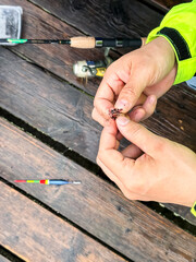 Vertical photo of men's hands baiting a live worm bait on a fishing hook