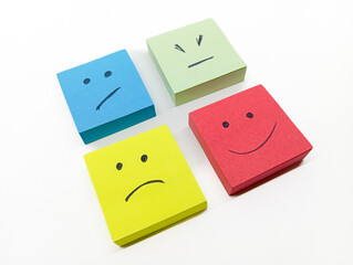 four colored sticky notes with hand-drawn faces representing various emotions, arranged on a white...