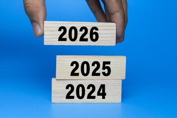 male hand put wooden blocks with year 2024, 2025, and 2026 isolated on blue background