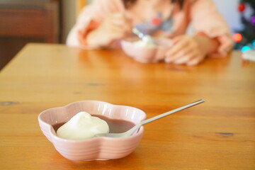 Child enjoying traditional Japanese yokan dessert with cream topping in a pink flower bowl on a wooden table, family snack moment.