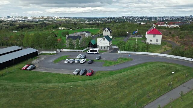 Aerial of Arbaer Museum Reykjavik with Icelandic turf houses and parking area. Stunning 4K video showing traditional architecture and cultural landscape.
