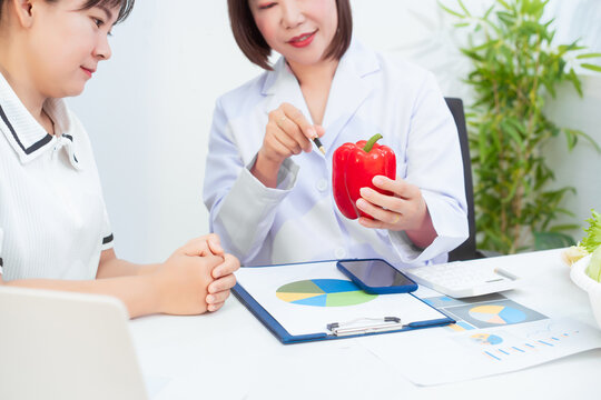Professional Asian female nutritionist giving nutritional counseling to female patient sitting at clinic table discussing diet, health goals, meal plans and strategies for long-term wellness