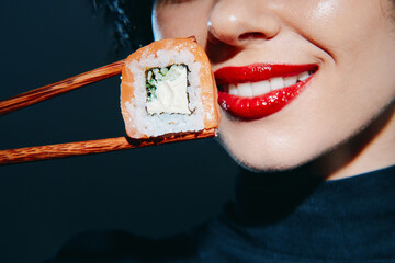 A smiling woman with red lips holding sushi with chopsticks, showcasing vibrant colors and a...