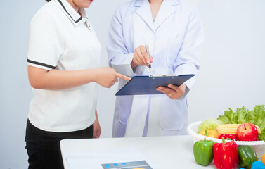 Professional Asian female nutritionist giving nutritional counseling to female patient sitting at clinic table discussing diet, health goals, meal plans and strategies for long-term wellness