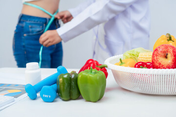 A middle-aged Asian female dietitian conducts a health consultation with a middle-aged Asian female patient at a table, focusing on weight loss, waist measurement, BMI, diet control,overall wellness
