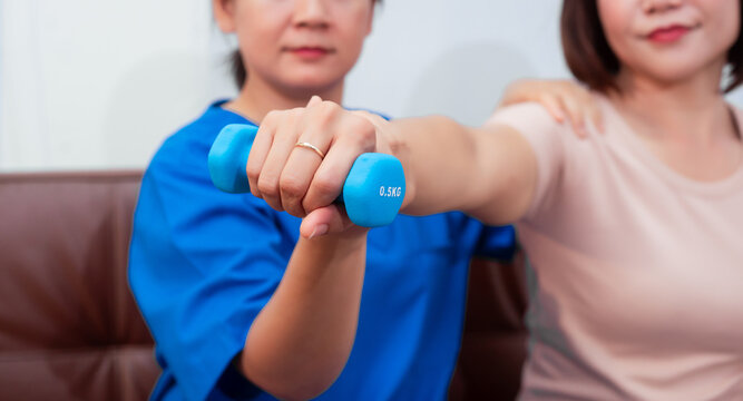 Young Asian nurse assisting middle-aged female patient on a couch doing physical therapy, focusing on muscle strengthening, rehabilitation, stretching,shoulder pain management in healthcare facility - Powered by Adobe