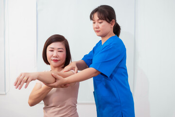 Obraz premium Young Asian nurse assisting middle-aged female patient on a couch doing physical therapy, focusing on muscle strengthening, rehabilitation, stretching,shoulder pain management in healthcare facility