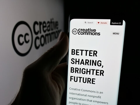 Stuttgart, Germany - 08-22-2025: Person holding smartphone with web page of US organisation Creative Commons (CC) on screen in front of logo. Focus on center of phone display.