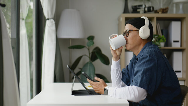 Asian man working from home on his tablet while sipping coffee. - Powered by Adobe